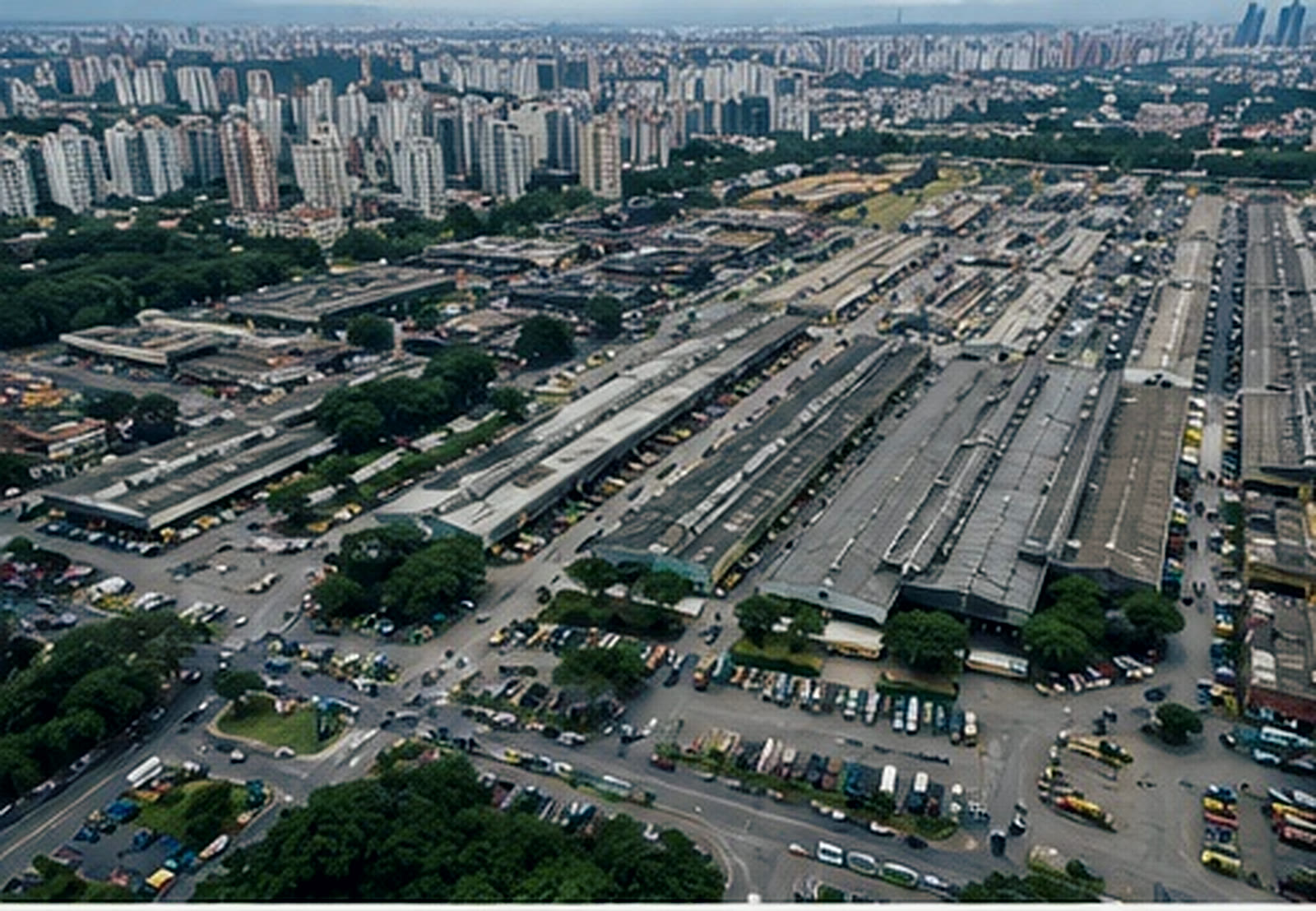 Vista aérea de um entreposto atacadista de hortifrúti, com galpões enfileirados e a cidade ao fundo